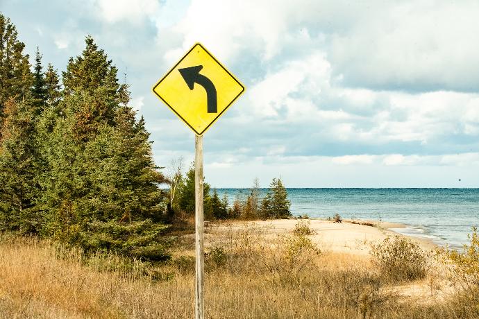 blue and white arrow sign near green trees and body of water during daytime